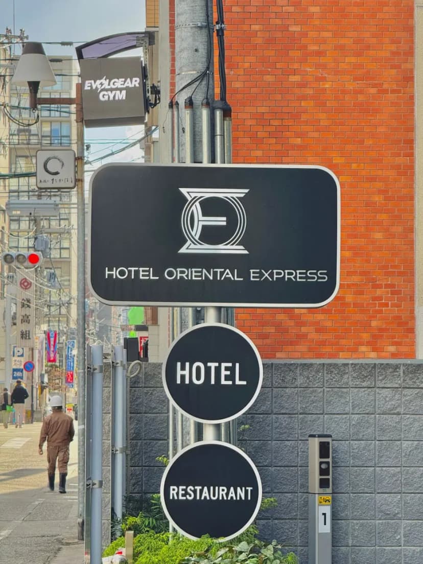 The clear black signage for HOTEL ORIENTAL EXPRESS FUKUOKA NAKASUKAWABATA on the building's exterior.