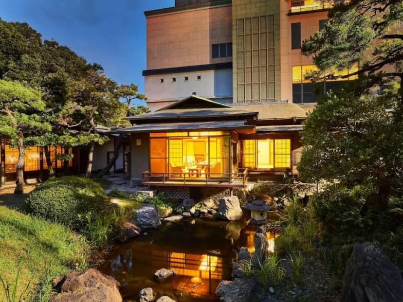 An outdoor onsen bath surrounded by nature, with steam rising from the water.